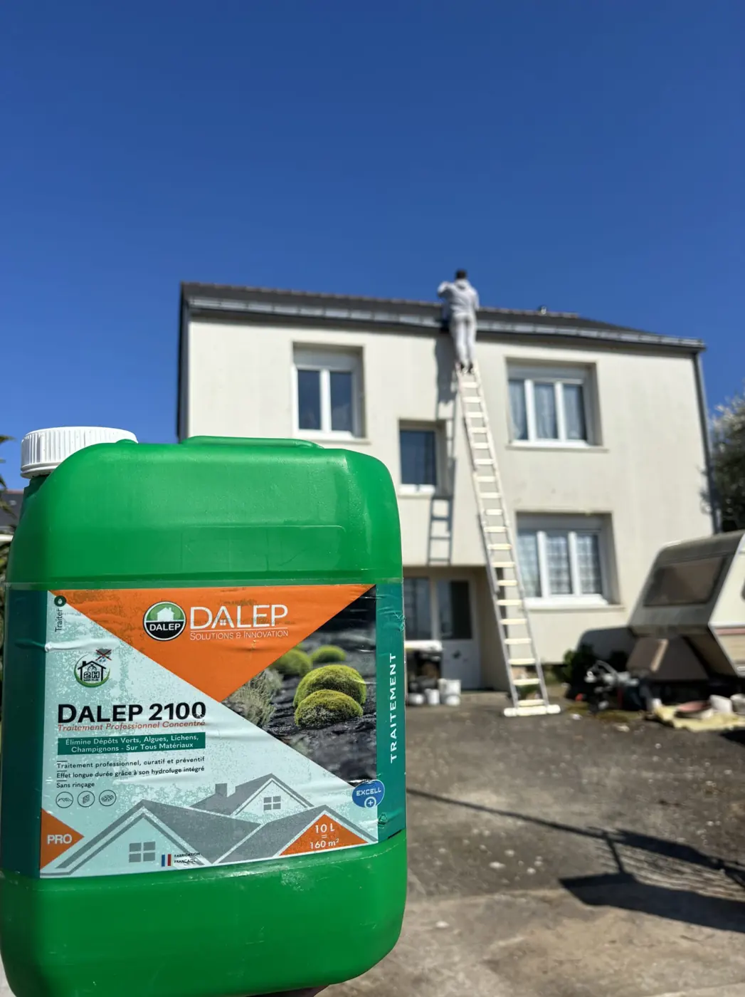 Bidon de DALEP 2100 au premier plan, le couvreur de Protech Toiture sur l'échelle, au bord du toit